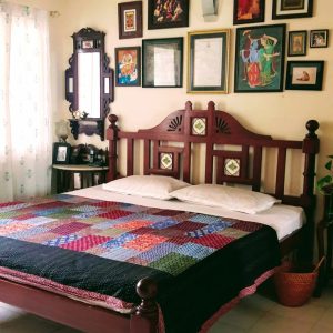 Traditional wooden bed with decorative headboard and colorful patchwork quilt, set in a cozy bedroom adorned with framed artwork and a side table.