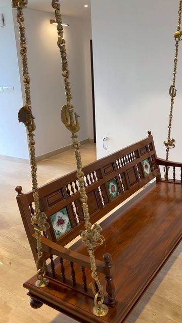 87bc93c8-1aa4-471c-803e-7b3435fcc9c7 Traditional wooden swing (jhoola) with brass chains and hand-painted tile inlays, suspended in a modern indoor space.