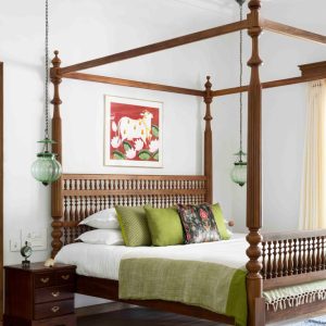 Traditional four-poster wooden bed with green bedding and hanging pendant lights in a bright, airy bedroom.