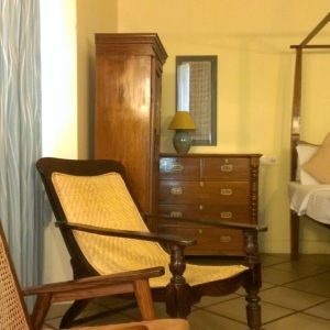 Traditional wooden Indian bedroom furniture set including cane-back chairs, a chest of drawers, a wardrobe, and a four-poster bed.