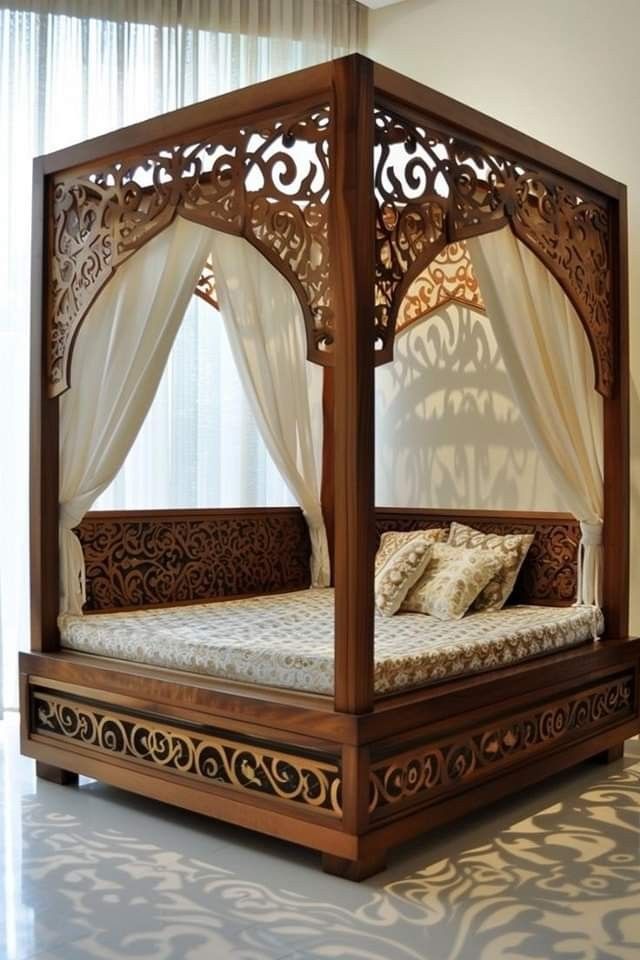 e9559f35-feb8-4316-8f5c-4e2aaa142e7b Intricately carved wooden canopy bed with sheer white drapes and traditional patterned bedding, placed in a modern, sunlit room.